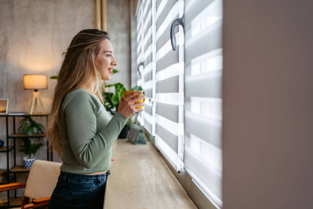 istock Young Woman Drinking Coffee While Looking Out The Window At Home 2159356490