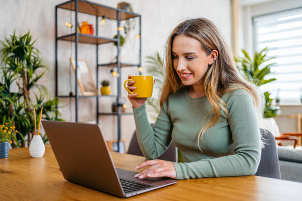 istock Young Woman Drinking Coffee And Working On A Laptop While Sitting At The Kitchen Table At Home 2159356830