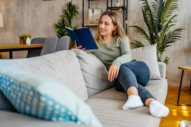 istock Young Woman Reading A Book While Sitting On The Sofa At Home 2159357021