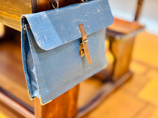 A close-up view of a vintage leather satchel hanging on the back of a wooden bench
