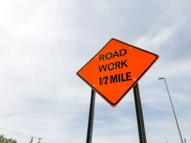 istock Orange color road work sign over cloudy sky 2159365821