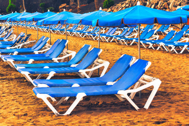 Beach with many blue and white beach chairs and umbrellas. . The chairs are arranged in rows and the umbrellas are open. Inviting relaxation and enjoyment.