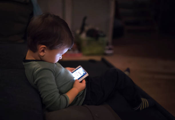 istock Cute boy sitting on bed watching something on smartphone. Children's screen time. 2159367713
