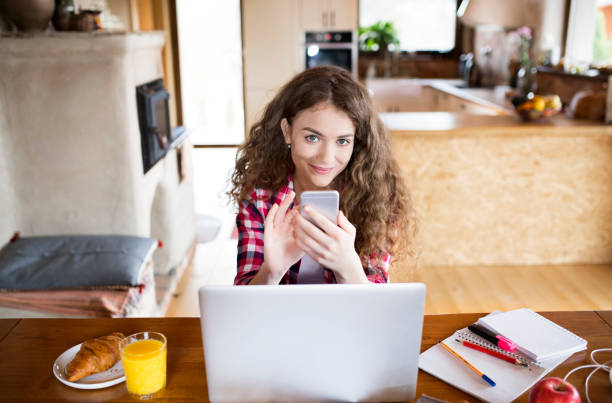 istock A beautiful university student is writing her thesis on a laptop, sitting at home at table and scrolling on smartphone. 2159369235
