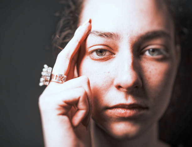 Portrait of a young, self-confident woman. She is looking directly at the viewer. She holds her hand thoughtfully to her face.