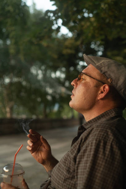 istock Handsome man smoking a cigarette and drinking coffee in the park 2159390199