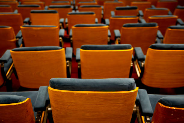 istock Several wooden chairs with blue cushions lined up back to back forming an audience without people 2159399320