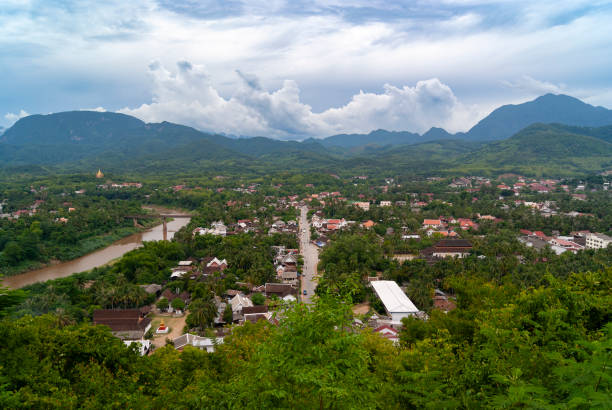 A picturesque view from Mount Phousi, a prominent hill in Luang Prabang, Laos. The area is covered in lush greenery and is a popular spot for tourists to enjoy panoramic views of the city and surrounding landscapes. The area is known for its beautiful sunsets and the historic Wat Chom Si temple located at the summit. Visitors often climb the steps leading to the top to experience the serene atmosphere and scenic vistas.