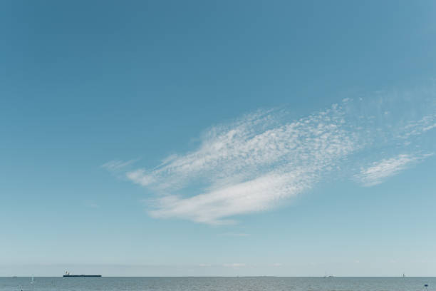 minimalistic shot of a ship on the horizon with clouds and blue sky