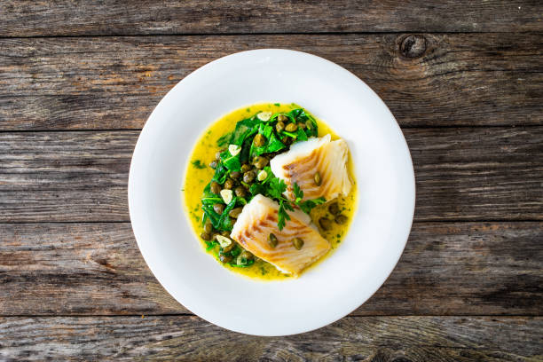 Fish dish - fried cod with spinach and capers in saffron sauce on wooden table