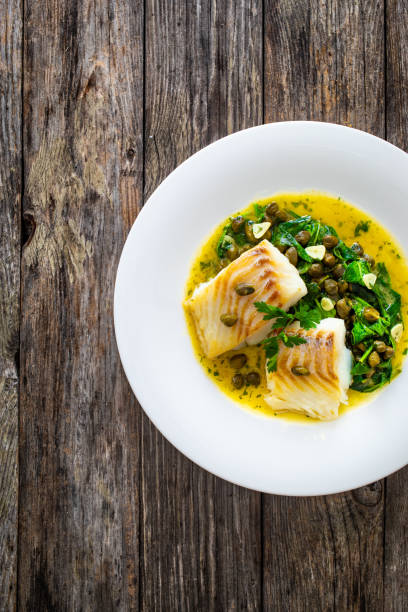 istock Fish dish - fried cod with spinach and capers in saffron sauce on wooden table 2159414044