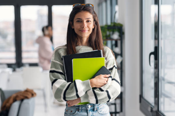 istock Attractive young designer woman holding some folders and smartphone while looking at camera in a modern office 2159414391