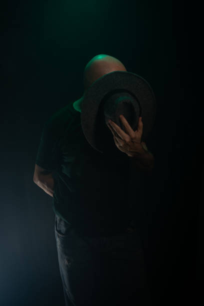 istock Mysterious man holding a hat in front of his face posing for the camera. Studio portrait. 2159416442
