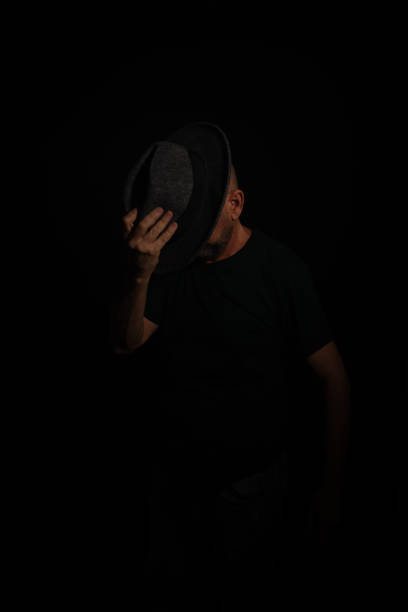 istock Mysterious man holding a hat in front of his face posing for the camera. Studio portrait. 2159416464