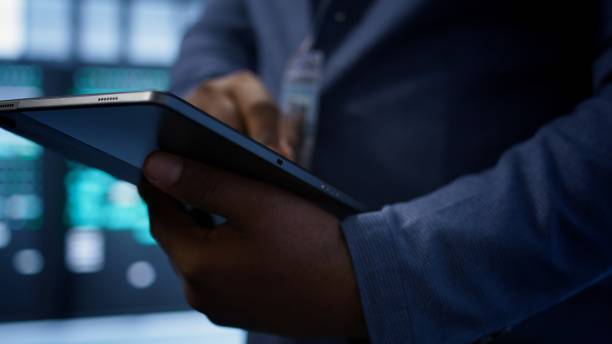 Software developer doing yearly maintenance using tablet to prolong data center equipment life span. Extreme close up of worker in server hub monitoring server infrastructure using device, camera B
