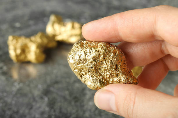 istock Woman holding gold nugget at grey textured table, closeup. Space for text 2159425594
