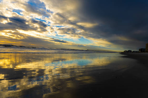 Jacksonville Beach sunrise: Golden rays streak over the Atlantic, painting the sky in pastel hues as waves whisper against the shore, welcoming a new day.
