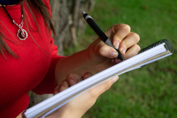 istock Girl in red coat taking notes with her pen in her notebook. Nature background 2159427807