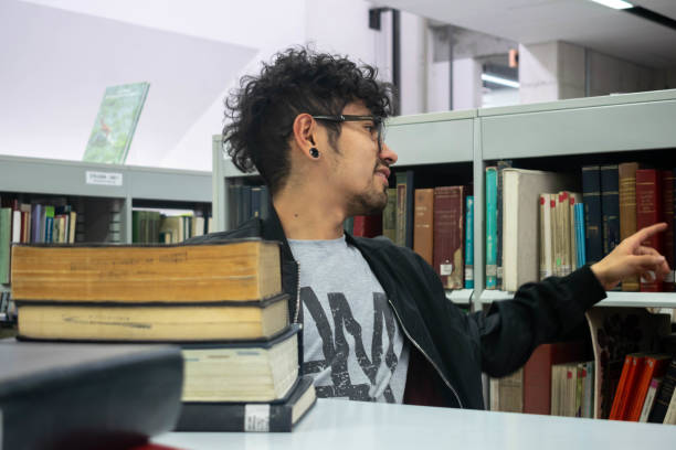 Curly-haired brunette student with glasses and piercing studying in the library. Back to school