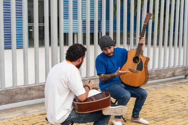 Two Musicians Discussing Guitar Techniques Outdoors Two musicians with guitars discussing and demonstrating guitar techniques outdoors. acoustic guitar tattoos stock pictures, royalty-free photos & images