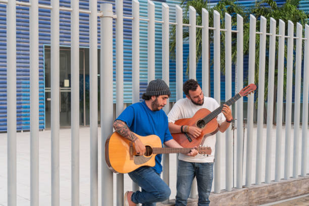 Two Men Playing Guitars Outdoors by Metal Fence