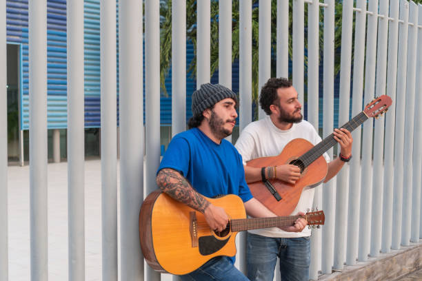 Latin Men Playing Guitars Outdoors by Metal Fence