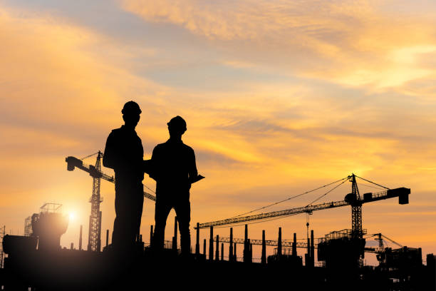 istock Silhouette of Engineer and worker checking project at building site, Engineer and builders in hardhats discussing on construction site 2159444533