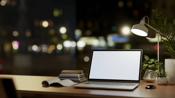 istock A laptop computer mockup on wooden table against the window with city nightlight view. 2159452102