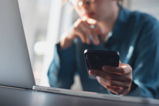 istock Close up, pensive business woman working on laptop computer, thinking of problem solution, and using mobile phone at office. Woman using smartphone and searching the ideas on laptop, surfing tne internet on office table, internet technology 2159453842