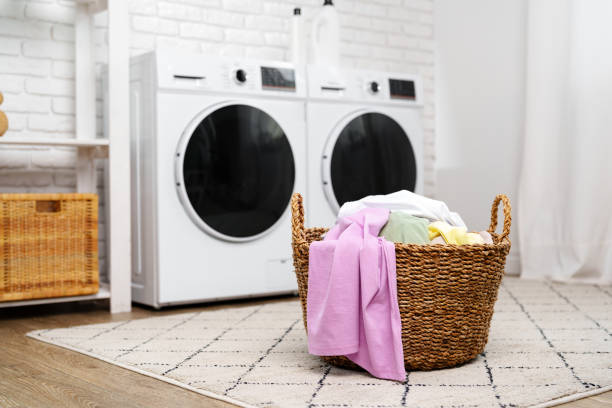 istock Laundry Basket With Clean Clothes in Front of Modern Washing Machines 2159464632