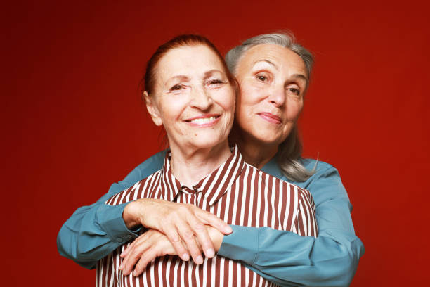 istock Two elderly women friends hugging on red background. 2159472007