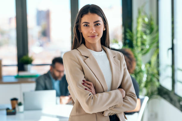 Beautiful young business woman standing while smiling looking at camera in the office Portrait of beautiful young business woman standing while smiling looking at camera in the office well dressed stock pictures, royalty-free photos & images