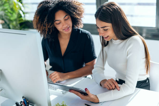 istock Two attractive business women talking and working with computer and digital tablet in coworking place 2159472627
