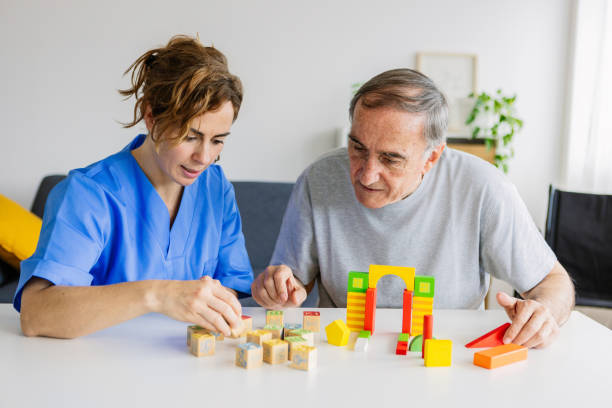 Caregiver and senior man playing wooden shape puzzles for dementia prevention stock photo
