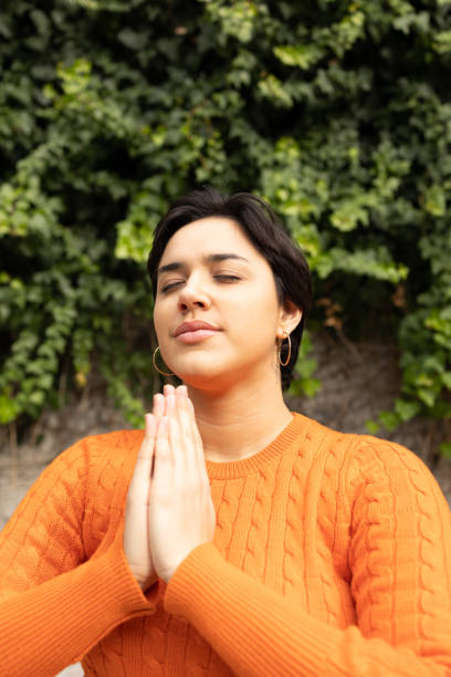 istock Young woman with hands clasped meditating against ivy wall 2159487757