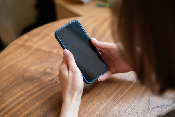istock A woman uses a smartphone with a blank black screen at the table in cafe 2159488252