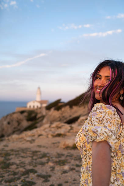 Young woman is enjoying the view of the sunset at the coast with a lighthouse in the background