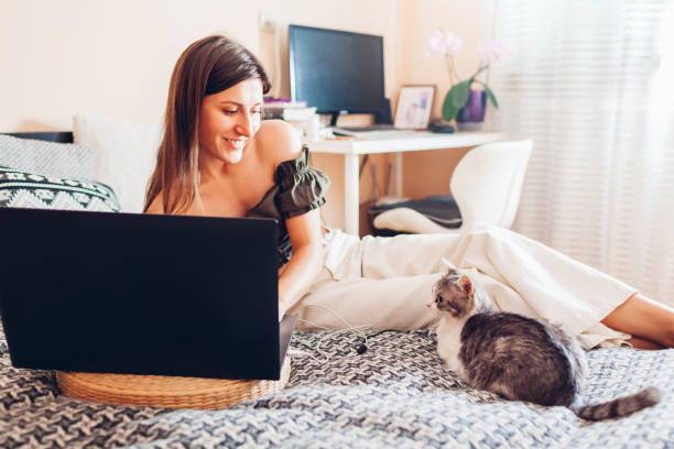 istock Smiling woman working online from home using laptop. Cat lying on couch by owner. Curious pet looking at screen 2159490895