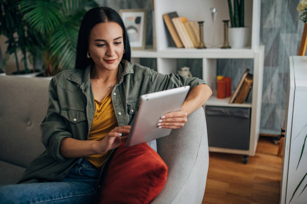 Woman using tablet on couch in modern living room setting.