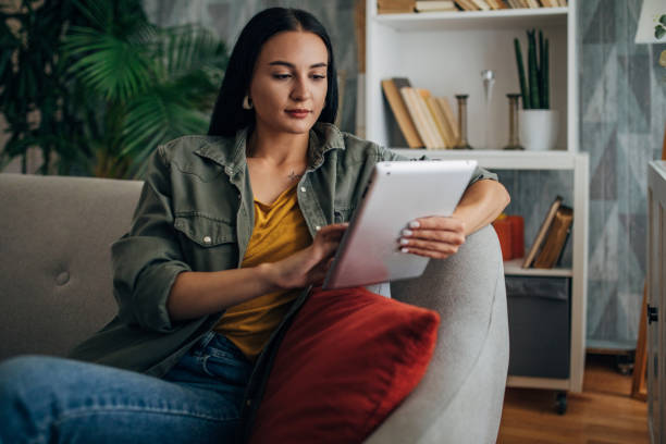 istock Woman focused on using a tablet on couch with red pillow. 2159493505