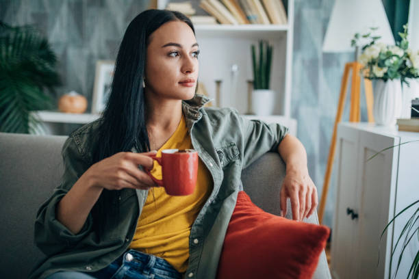 istock Woman holding red cup while sitting on grey couch. 2159496201