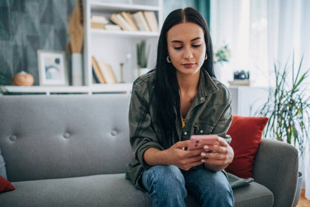 istock Woman sitting on grey couch looking at her phone. 2159497354