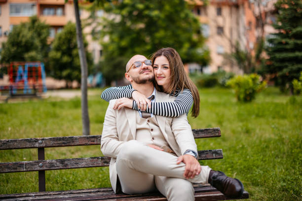 Beautiful young well-dressed couple embracing on a park bench in a public park outdoors.