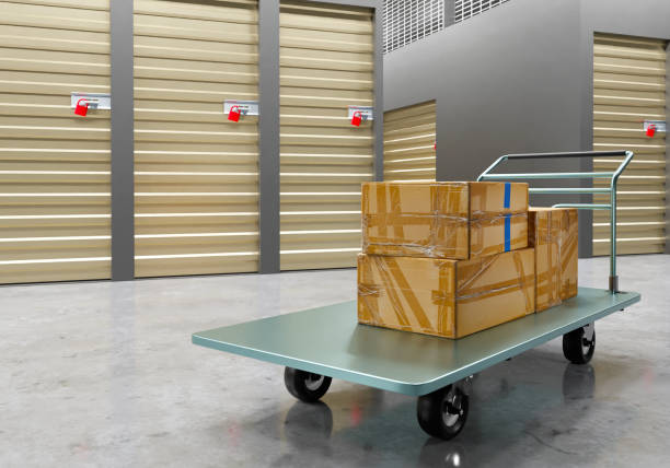 istock Sweet cart. Cargo trolley with boxes. Flat trolley for transporting crates around warehouse. Cargo trolley on concrete floor. Walls with closed doors in background. Cart in storage company. 3d image. 2159506030