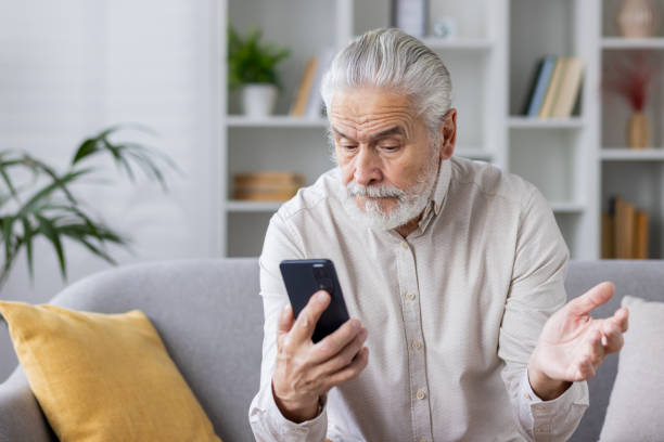 istock Senior man using smartphone on sofa looking confused and frustrated at home 2159509815