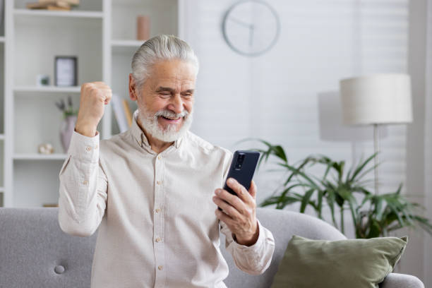 istock Excited senior man celebrating success while using smartphone at home 2159510090