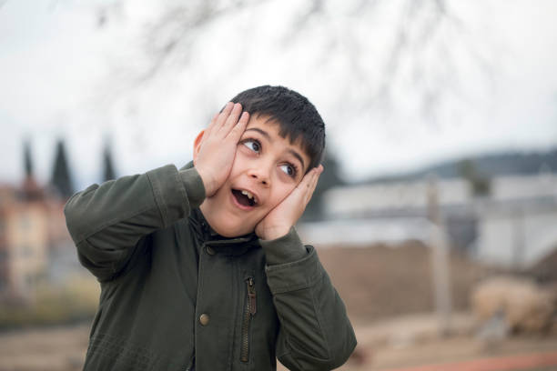 Portrait of cute little Asian boy at his desk, looking to his right with surprise expression over white background.