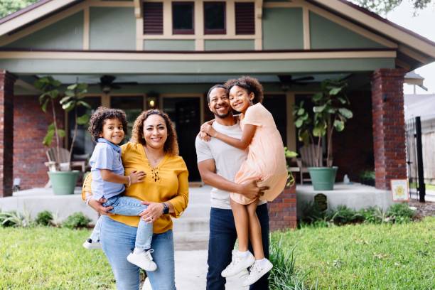 Portrait of parents holding their two kids in front of the house Portrait of multiracial parents holding their kids in front of the house home ownership stock pictures, royalty-free photos & images