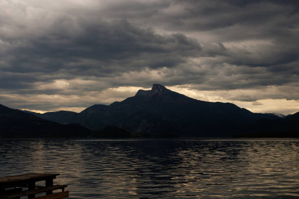 A serene dusk scene over a tranquil lake with a majestic mountain backdrop under moody clouds