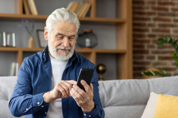 istock Senior man smiling while texting on his smartphone at home 2159513979
